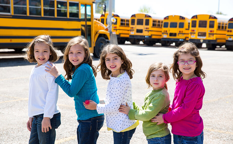 young girls in front of schoolbuses